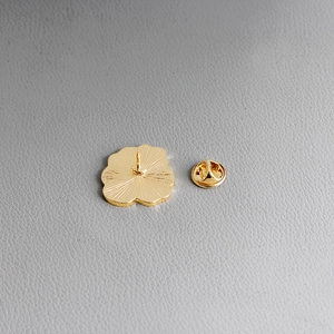 Close-up of golden metal flower brooch back featuring a butterfly clasp on grey leather