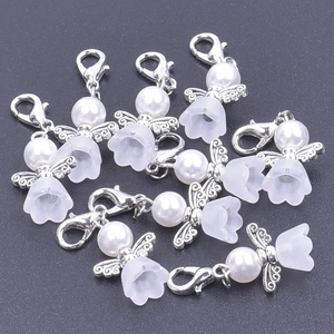 Close-up of angel favor charms with white pearls and silver wings on a dark surface