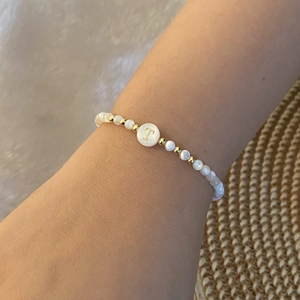 Detailed shot of beaded bracelet with white shell beads and golden letter T on the wrist