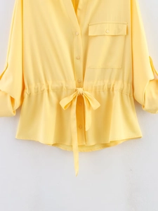 Detail of yellow long sleeve shirt showing V-neck, chest pocket, and drawstring waist