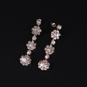 Elegant rose gold drop earrings with tiered crystal petals on a matte black surface