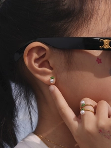 Detailed close-up of golden pearl earrings and crown ring set worn by model