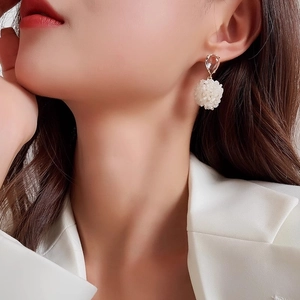 Close-up of elegant white floral pearl earrings on model wearing a white suit