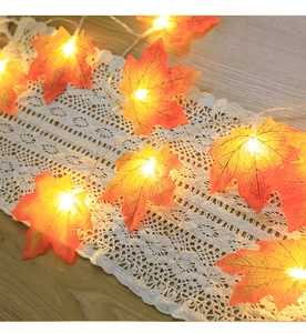 Close-up of LED maple leaf fairy lights with warm glow on a white lace runner