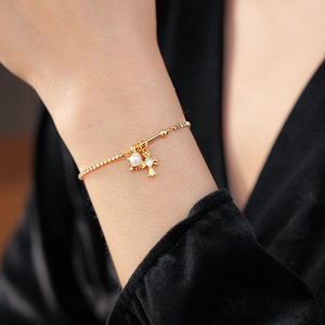 Détail d'un bracelet croix doré avec diamants et perles porté sur un tissu en velours noir