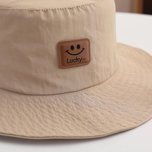 Close-up of khaki sun hat featuring a brown leather patch with a black smiley face icon