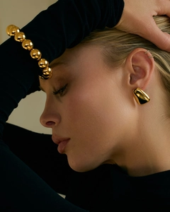 Détail de boucles d'oreilles trapèze dorées 18 carats et bracelet perlé sur un mannequin