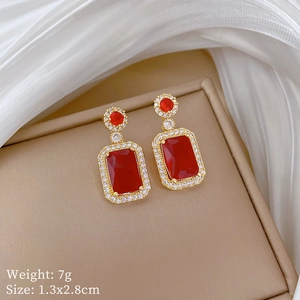 Detail of gold earrings with rectangular red gemstones and micro-pave white zircon stones
