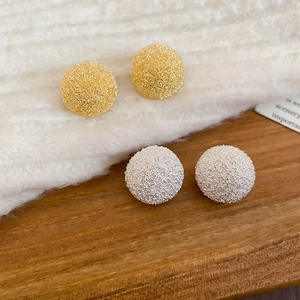 Detailed view of gold and silver textured round stud earrings on fabric and wood