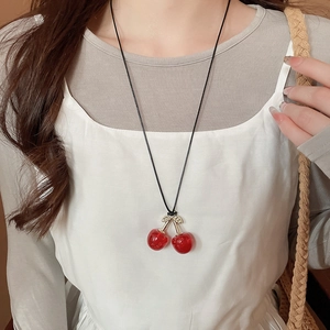 Close-up of red cherry pendant necklace with gold leaves and black cord on a model