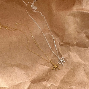 Detailed view of gold and silver bow tie pendant necklaces on brown paper background