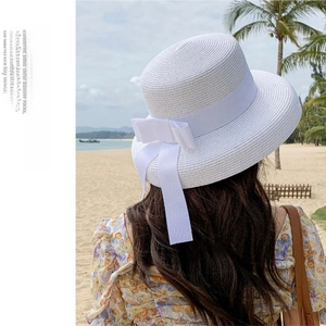 Back view of a white straw hat with a large bow ribbon on a sunny tropical beach scene