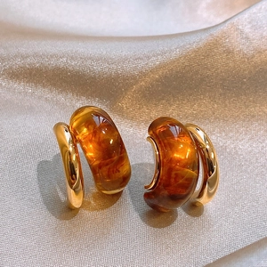 Detailed close-up of C-shaped amber resin earrings with golden metal on silk fabric