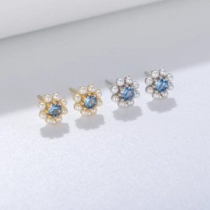 Macro shot of silver and gold flower earrings with blue zircon and elegant pearls