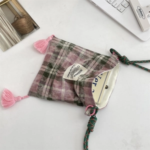 Macro detail of plaid fabric bag featuring pink tassels and a woven shoulder strap