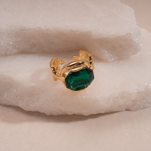 Detail of vintage gold-plated ring set with emerald-cut green stone on white stone base
