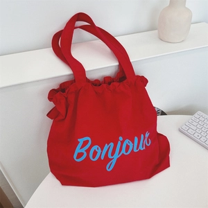 Detail of red canvas tote bag with blue Bonjour lettering and drawstring closure