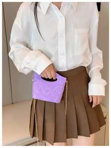 Dettaglio mini borsa viola trapuntata con catena dorata indossata su camicia bianca