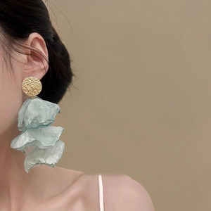 Elegant mint green chiffon flower drop earrings with a textured gold disc on a model