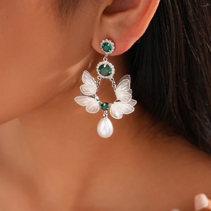 Silver butterfly drop earring with green rhinestones and white pearl on model's ear
