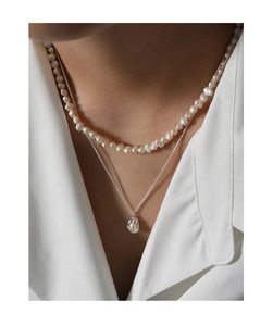 Detail view of a layered S925 silver necklace set with shell pearls on a white shirt