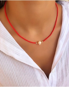 Close-up of a handmade red seed bead necklace with a single white pearl on a model