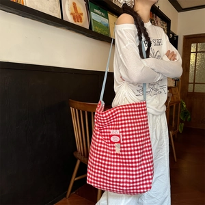 Red plaid tote bag with embroidery detail worn by a model in a retro vintage shop