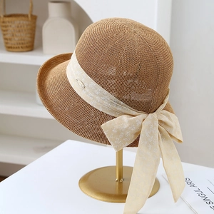 Close-up of woven straw hat featuring a floral ribbon bow and elegant metal emblem
