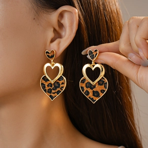 Close-up of heart-shaped leopard print earrings with gold frames on a female model