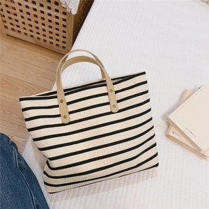 Close-up of black and white striped canvas tote with khaki leather handles and rivets