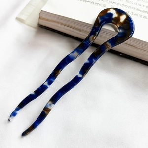 Close-up of wavy U-shaped acetate hair pin with blue and brown marble texture on white cloth