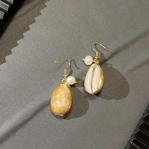 Detailed close-up of golden shell earrings with white pearl dangles on grey fabric