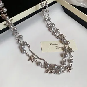 Double-layered gray pearl necklace with silver star pendants on a minimalist white tray