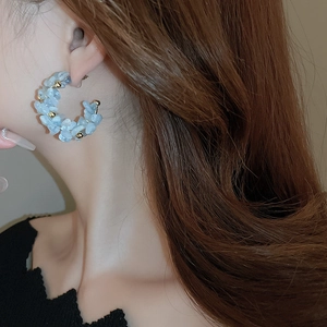 Close-up of C-shaped blue gemstone beaded earrings worn for a vacation style look