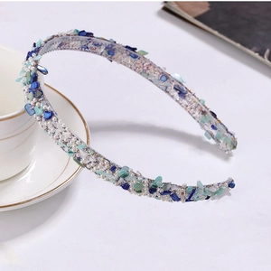 Detail of floral headband with blue and green stones and small pearls on a white desk
