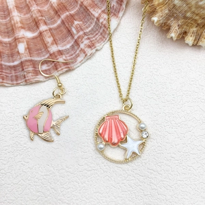 Flat lay of pink shell and starfish pendants with tropical fish earrings on white texture