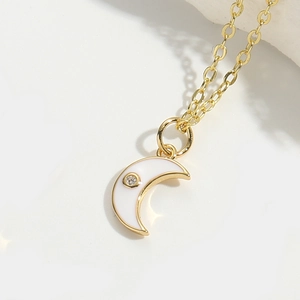 Detail of golden crescent moon pendant with white enamel and a single zircon crystal