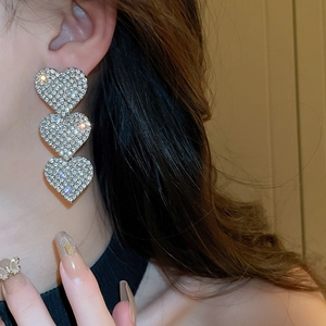 Close-up of triple heart drop earrings with glittering rhinestones worn by a model