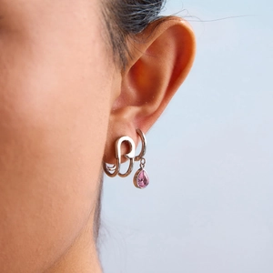 Close-up of titanium steel earrings featuring a pink teardrop gemstone and silver hoop
