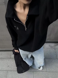 Outdoor street view of black quarter-zip sweatshirt paired with ripped light blue jeans