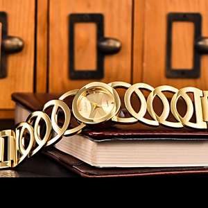 Elegant gold quartz bangle watch with hollow links displayed on books by a vintage cabinet