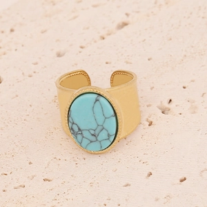 Vue macro d'une bague large dorée avec pierre turquoise ovale et anneau ouvert