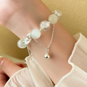 Detailed macro view of light green crystal beads and polished silver bell charm on bracelet
