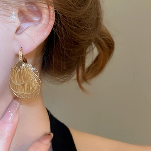 Close-up of golden hollowed heart petal earrings with a brushed metallic texture