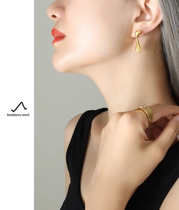 Detalle de los pendientes de gota y el anillo texturizado en acero dorado de 18K