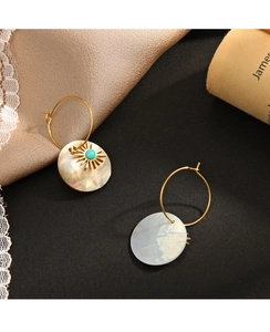 Close-up of shell earrings with sunburst pattern and turquoise stone on silk fabric