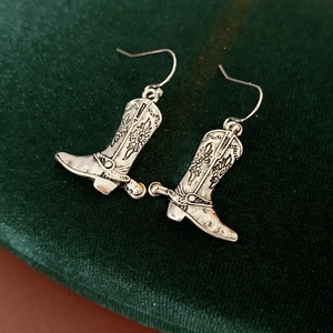 Détail macro de boucles d'oreilles bottes de cowboy argentées avec gravures sur velours