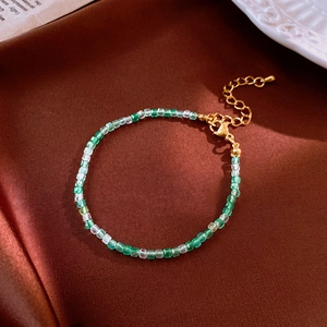 Detail of green and white beaded bracelet with gold extension chain on brown silk fabric