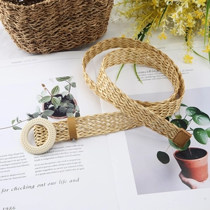 Detail view of a woven straw belt with a round buckle on an aesthetic lifestyle background