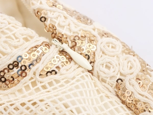 Macro shot of off-white knit mesh fabric with gold sequins and a teardrop zipper detail